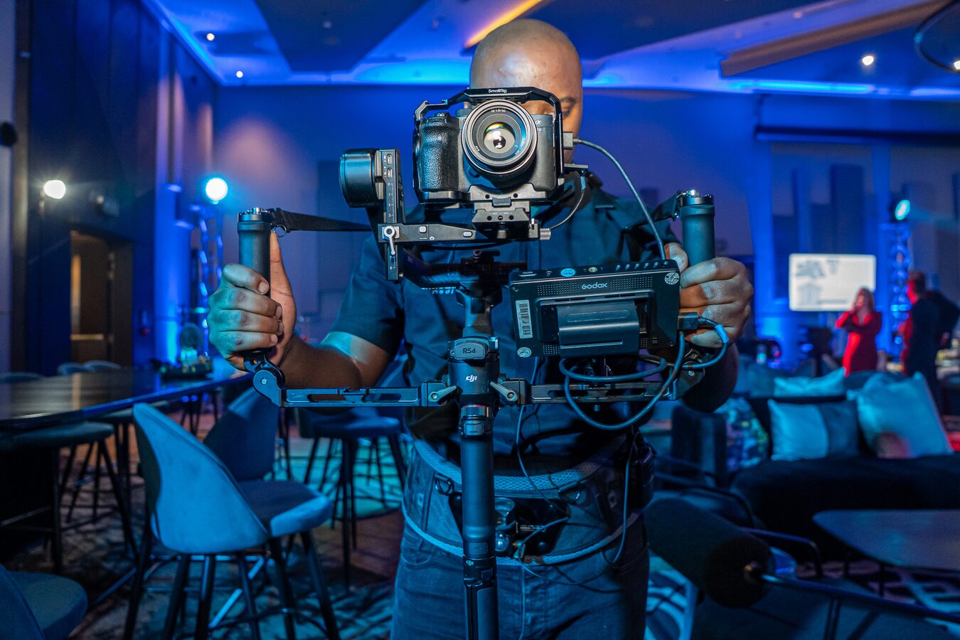 Videographer operating a gimbal-mounted camera in a blue-lit conference venue