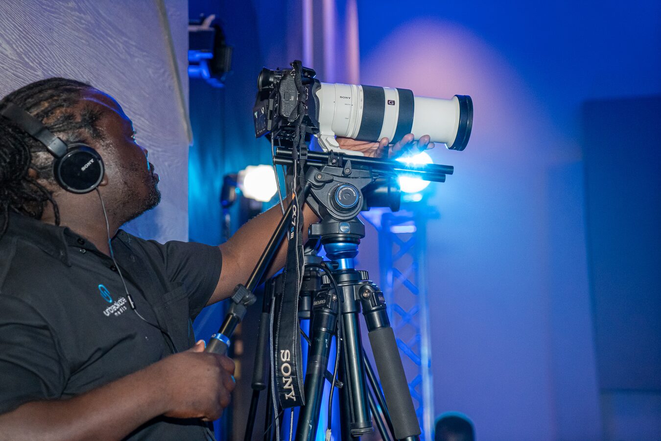 Camera operator adjusting a Sony cinema camera on a tripod under blue stage light